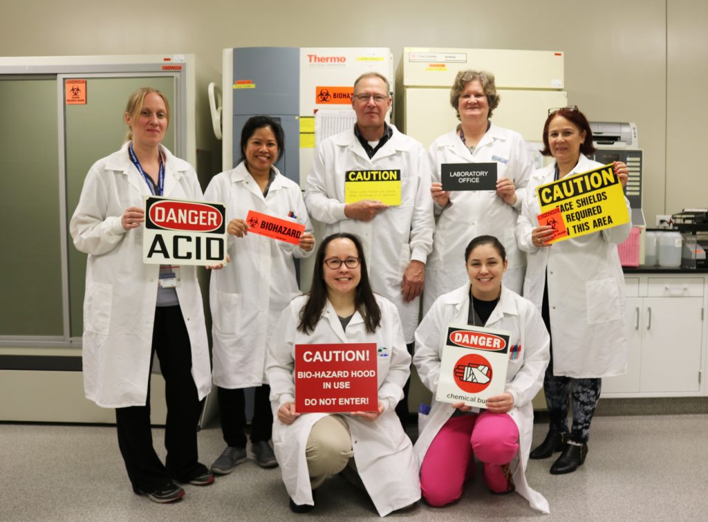 Patricia Bolivar with lab partners holding various signs including mostly caution signs.